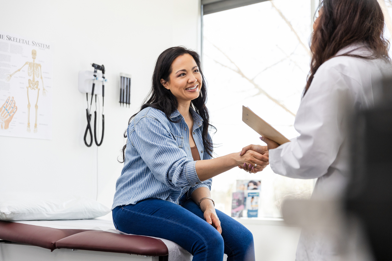 female patient shaking hands with female doctor in exam room